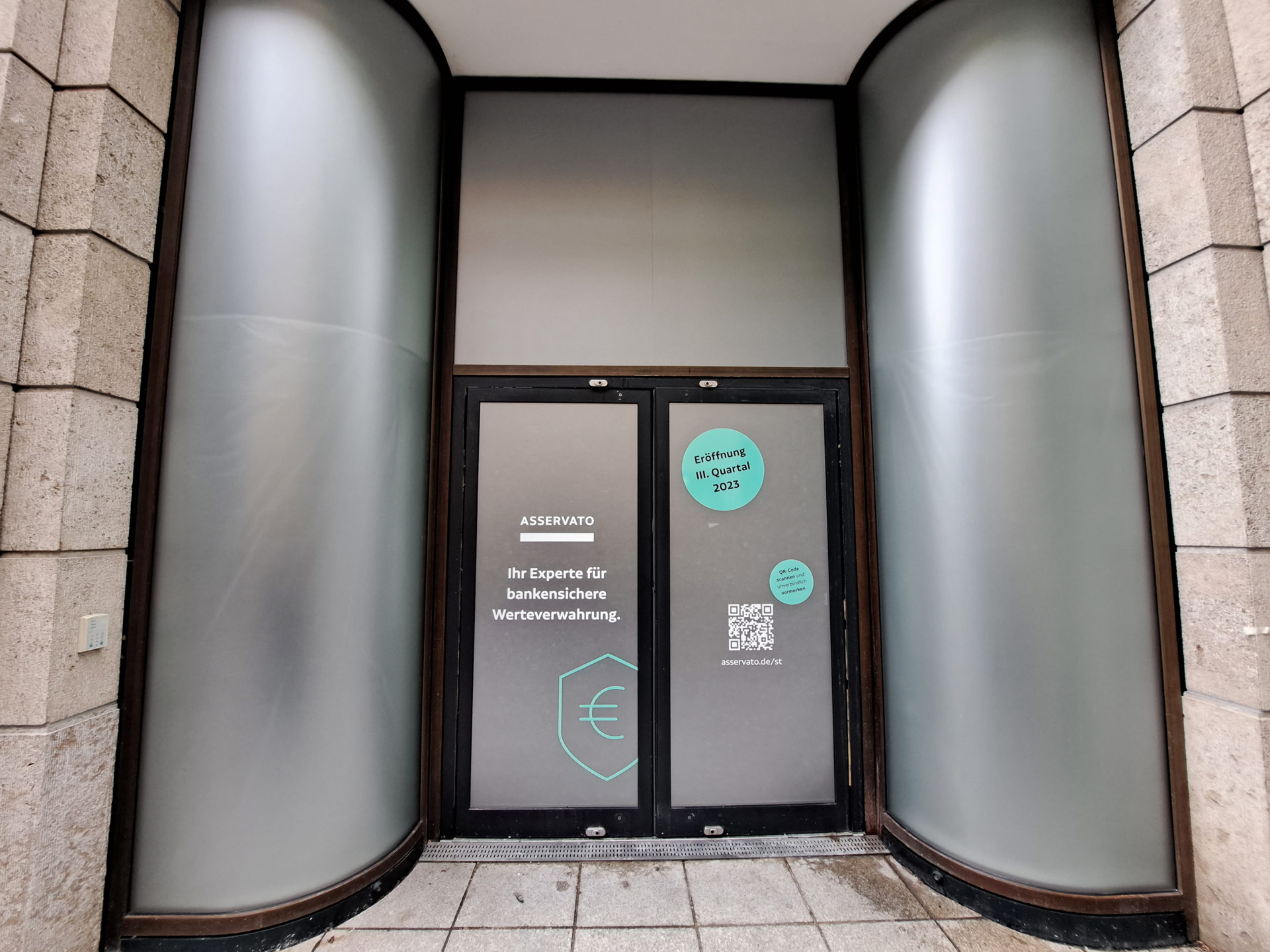 Eine Eingangstür mit moderner Beschriftung in einem Gebäude und grauer Fassade