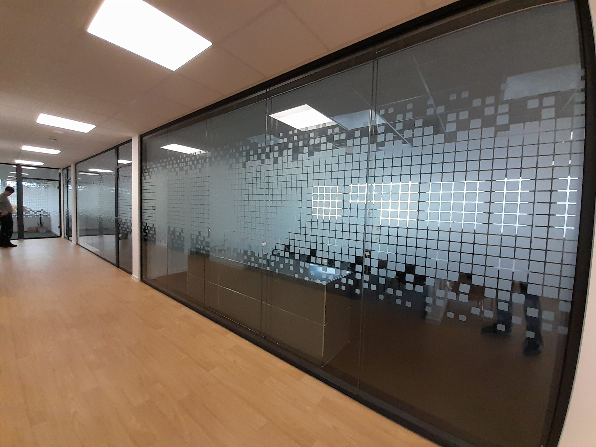 Eine moderne Glaswand mit quadratischen Mustern in einem hellen Büroflur.