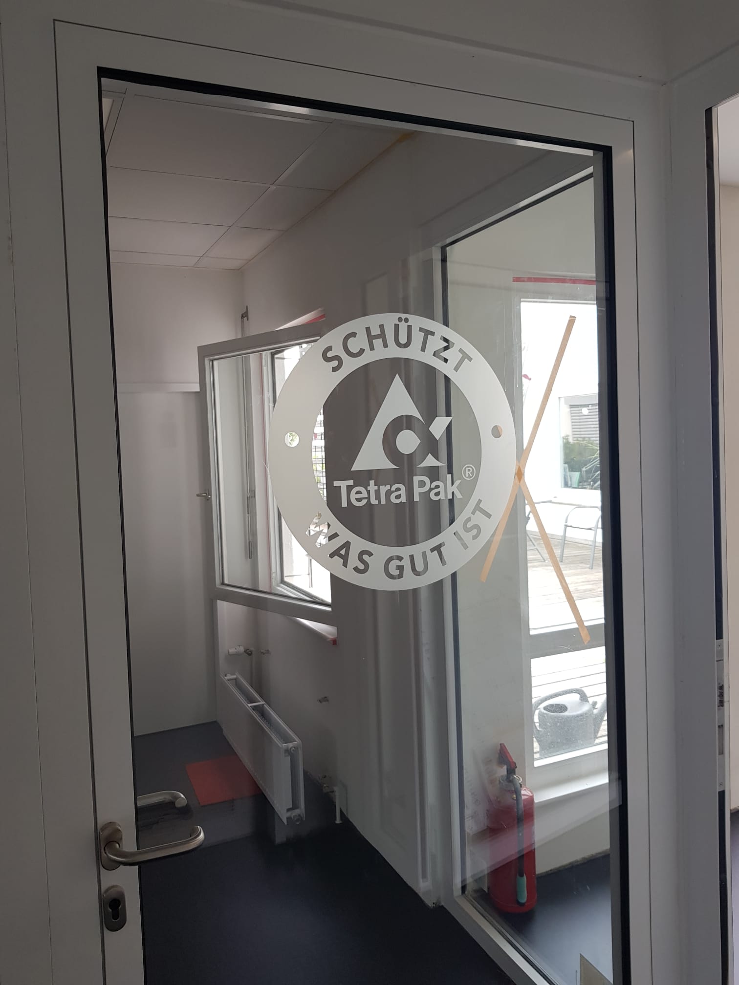 Ein fensterloser Raum mit weißem Interieur und einem Tetra Pak Logo auf der Scheibe, daneben ein Feuerlöscher.