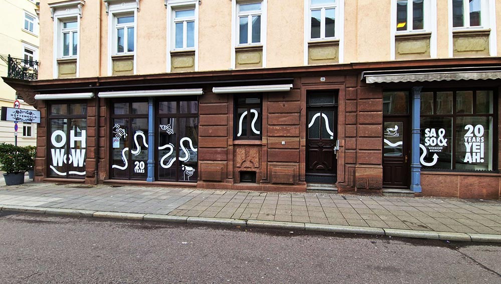 Beiges und braunes Ladenlokal mit Schaufenstern, weisser Typografie und Markise